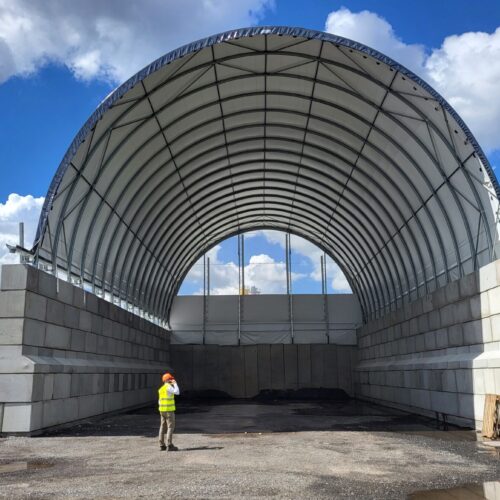 Duża hala łukowa z betonowymi ścianami bocznymi podczas budowy, przeznaczona na kruszywa budowlane