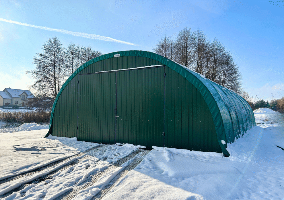 Hala namiotowa o łukowej konstrukcji z zielonymi ścianami i dużymi bramami wjazdowymi, ustawiona na zaśnieżonym terenie. Obiekt stanowi funkcjonalne zaplecze magazynowe, dobrze sprawdzające się także w warunkach zimowych.