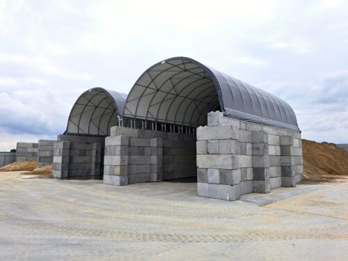 Dwie hale namiotowe z solidnymi betonowymi ścianami, wykorzystywane do przechowywania piasku i kruszyw. Konstrukcja łukowa z wytrzymałym poszyciem chroni materiały przed opadami i wiatrem. Rozwiązanie idealne dla składów budowlanych i firm drogowych.