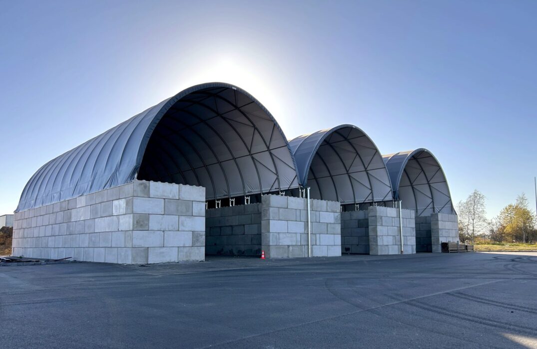 Na zdjęciu widoczne są trzy duże hale łukowe przeznaczone do składowania kredy. Konstrukcje opierają się na wysokich ścianach z betonowych bloków i posiadają ciemne poszycie namiotowe, chroniące wnętrze przed czynnikami zewnętrznymi. Całość zlokalizowana jest na utwardzonym placu.