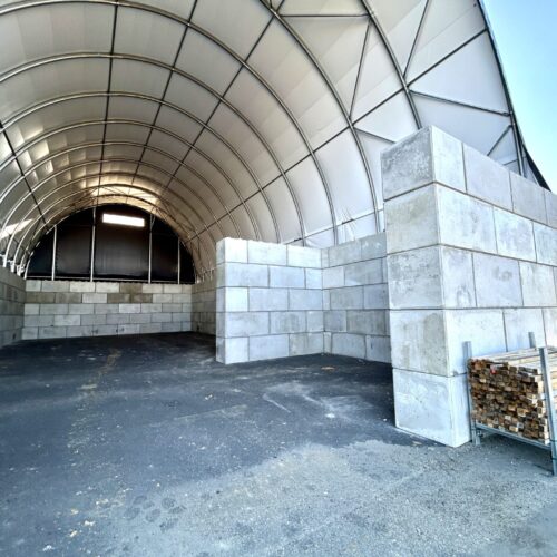 Nowoczesna hala łukowa z betonowymi ścianami wewnętrznymi, przeznaczona do składowania grysu i kruszywa. Konstrukcja z plandeki na stalowym szkielecie zapewnia trwałą ochronę materiałów przed warunkami atmosferycznymi. Obiekt przygotowany do użytkowania w branży budowlanej i drogowej.