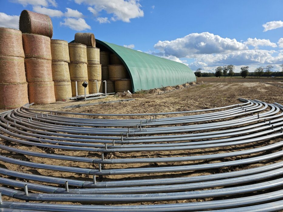 Hala tunelowa z zieloną membraną, wykorzystywana do przechowywania bel słomy lub siana ustawionych w wysokie stosy.