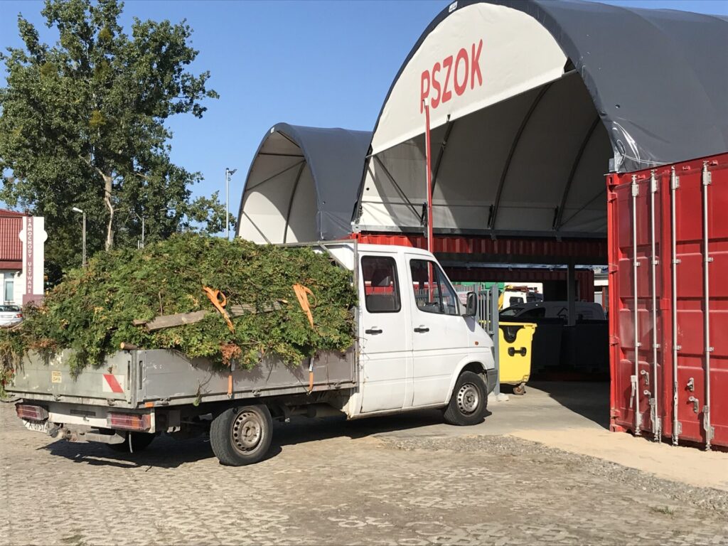 Biały wóz dostawczy z materiałami odpadowymi wjeżdża do hali łukowej punku selektywnej zbiórki odpadów.