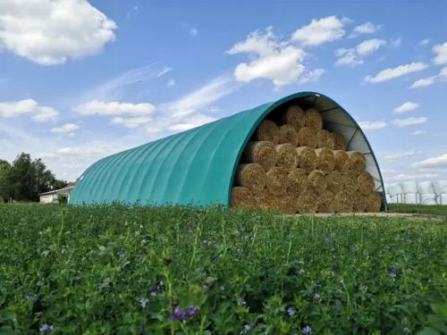 ukowa hala namiotowa 12x30 metrów z zielonym poszyciem, zaprojektowana do przechowywania pasz i materiałów rolniczych. Wewnątrz widoczna jest duża ilość bel słomy ułożonych w wysokie stosy.