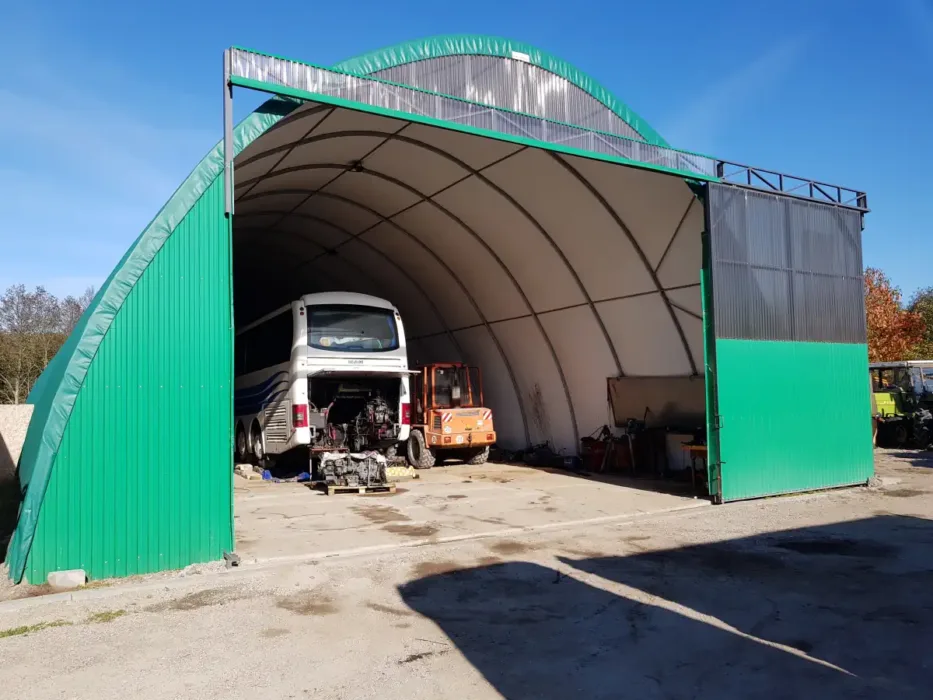 Przestronna hala namiotowa 12x30 metrów wykorzystywana jako garaż i warsztat dla pojazdów ciężarowych. W środku znajduje się autobus poddawany naprawie oraz inne maszyny serwisowe.