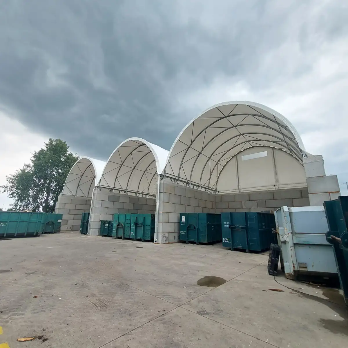 Trzy hale namiotowe z białym poszyciem, które służą do ochrony otwartych kontenerów z odpadami