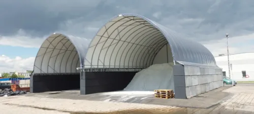 Dwie hale pokryte plandeką na betonowych bloczkach. Pod nimi znajdują się materiały sypkie.