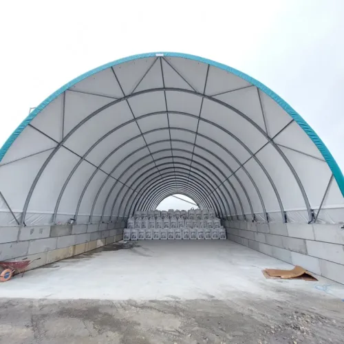 Wnętrze hali łukowej 15x30 z łukowym dachem i ścianami z betonowych bloków. Na końcu widoczne są palety z nawozami w big-bagach.