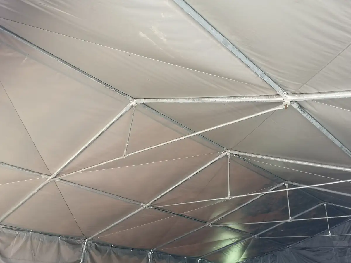 Zbliżenie na wewnętrzną konstrukcję dachu dwuspadowej hali namiotowej. Widoczna jest metalowa kratownica oraz napięte liny podtrzymujące poszycie z plandeki.