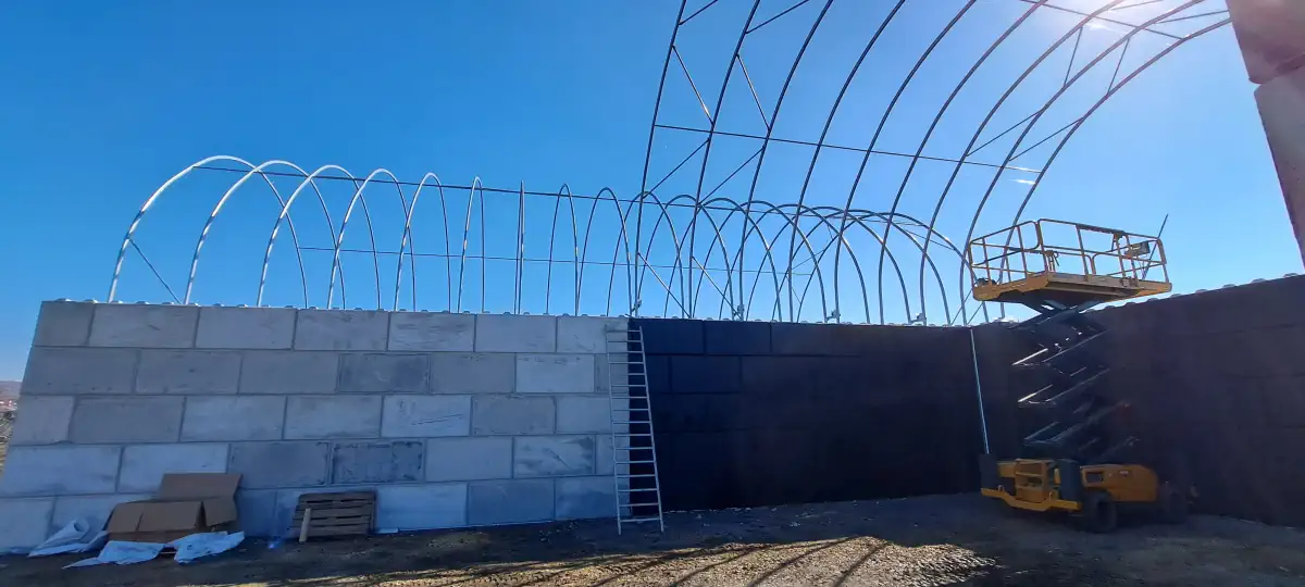Widok z dołu na stelaż hali namiotowej osadzonej na betonowych bloczkach. Widać windę budowlaną, która ułatwia prace nad halą namiotową.