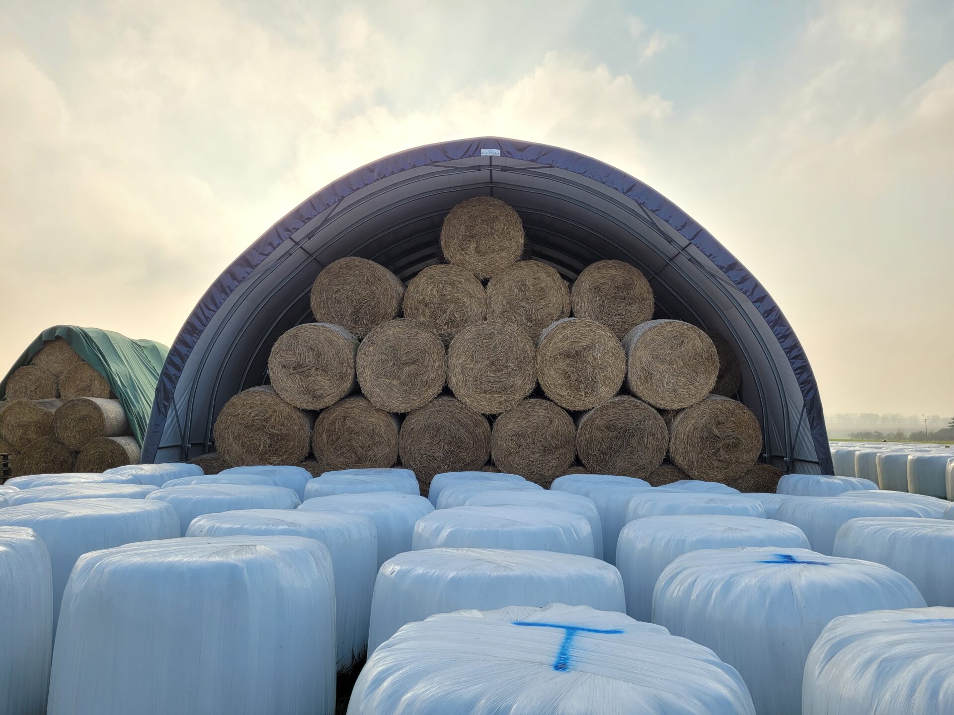 Front hali namiotowej w rozmiarze 10x20 w której składowane są baloty siana.