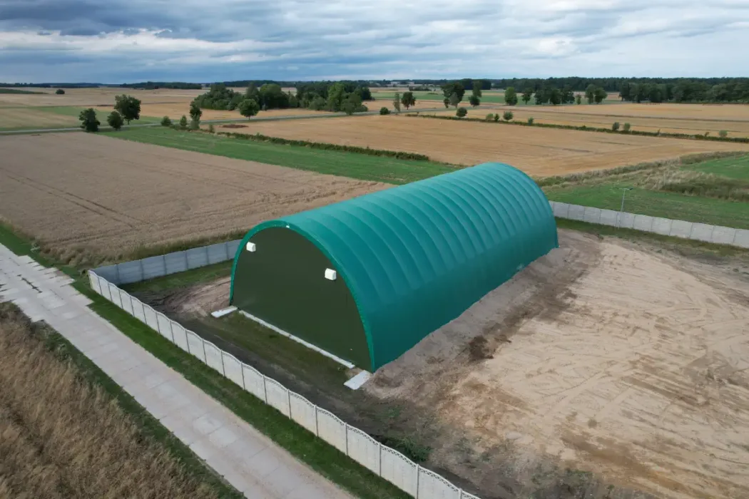 Duża zielona hala namiotowa o wymiarach 15x30 metrów, usytuowana w gospodarstwie rolnym. Poszycie wykonane z membrany PVC.