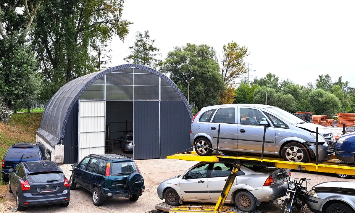 Hala z poszyciem membranowym stoi przy placu, na którym manewrują auta i laweta. Przesuwne drzwi otwierają dostęp do warsztatowo-magazynowego wnętrza.